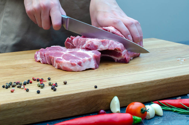 Γυναίκα στην κουζίνα, κόβει χοιρινό με μαχαίρι. Κρέας σε ξύλο κοπής, προετοιμασία μπριζόλας, προετοιμασία για τις διακοπές.jpg - Φωτογραφία, εικόνα