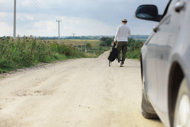 Een man loopt langs een landweg. Een lifter door het hele land. Een man stopt een passerende auto op de weg. - Foto, afbeelding