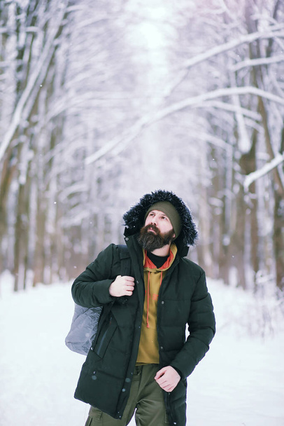Γενειοφόρος στο χειμερινό δάσος. Ελκυστικός χαρούμενος νέος με γενειάδα περπατάει στο πάρκο.. - Φωτογραφία, εικόνα