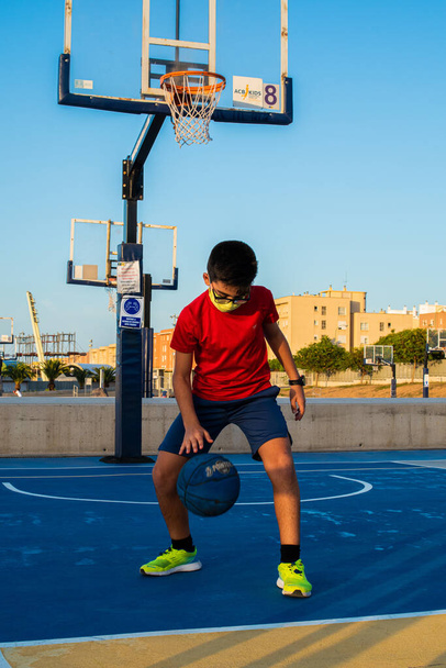 A vertical shot of a boy playing basketball wearing a sanitary mask-concept of the new normal - Foto, afbeelding