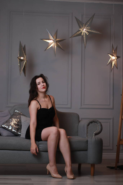 装飾的な大きな星とグレーの部屋にグレーのソファの上に黒のスキニードレスでセクシーな魅力的なブルネット。スタジオ撮影 - 写真・画像