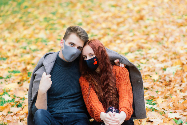 若いです赤い髪の女性は秋の公園で若い男と歩いている間に顔のマスクに置きます. - 写真・画像