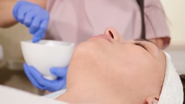 Szépségklinika koncepció. Női kozmetológus orvos készíti arc maszk eljárás keverés tálban ecsettel a beteg közelében. keverő alkatrészek üvegtálban. 4 k videó - Felvétel, videó