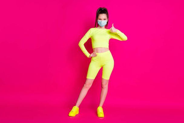 Full length photo of young woman dressed sportwear mask hand thumb up arm waist isolated pink color background - Фото, изображение