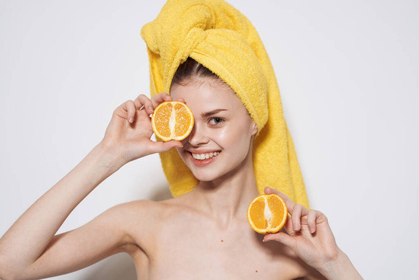 Mujer alegre hombros desnudos naranjas en las manos de una toalla amarilla en la cabeza sonrisa piel limpia - Foto, Imagen
