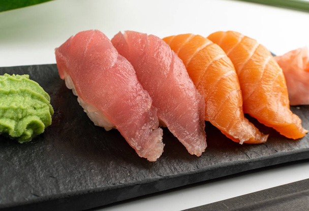 Macro foto de salmón nigiri sushi y maguro conjunto de susi de atún. Susi set rollos con pescado rojo crudo en placa de piedra oscura de cerca - Foto, Imagen