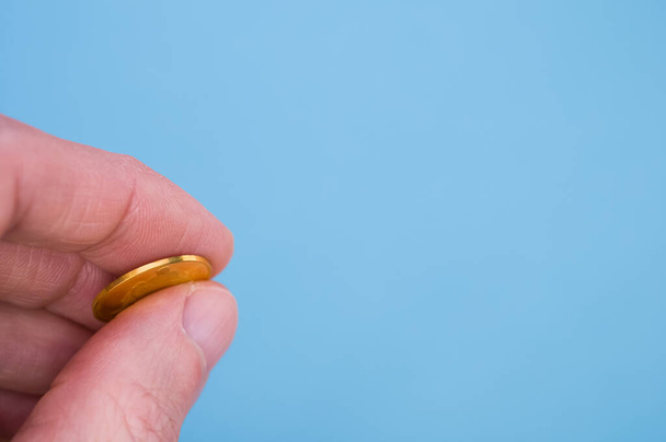 A closeup shot of a hand holding gold coin isolated on blue background - Φωτογραφία, εικόνα