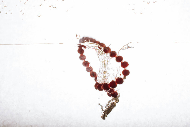 A high-speed shot of red beads bracelet on the clear water isolated on white background - Φωτογραφία, εικόνα