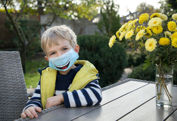 Ζωγραφισμένο αστείο χαμόγελο σε μια μπλε μάσκα προστασίας από ιούς. Μια διασκεδαστική μάσκα προσώπου DIY για ασφάλεια σε πανδημία ή καραντίνα. Χαμογέλα και να προσέχεις. Μην ανησυχείς, χρησιμοποίησε μάσκα. - Φωτογραφία, εικόνα