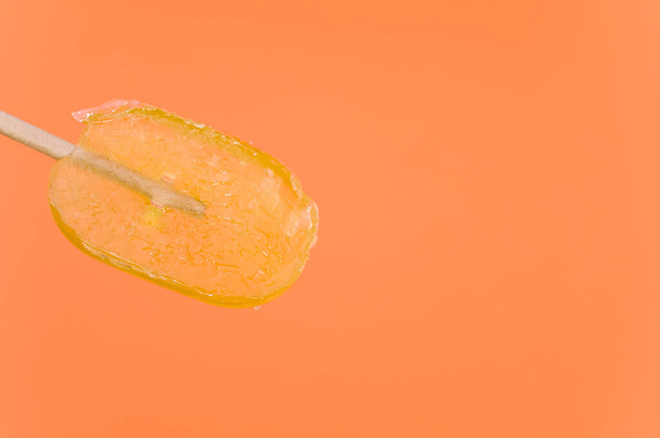 A closeup shot of an orange-flavored lollipop isolated on an orange background - Foto, imagen