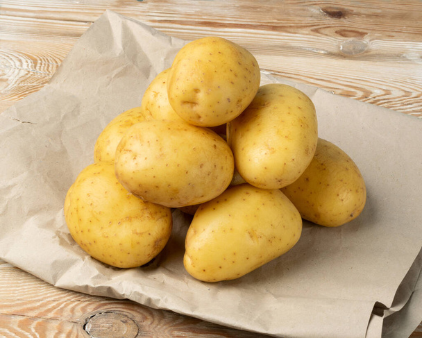 pile de pommes de terre entières crues sur fond en bois. Modèle de pommes de terre jaunes lavées sur papier vintage - Photo, image