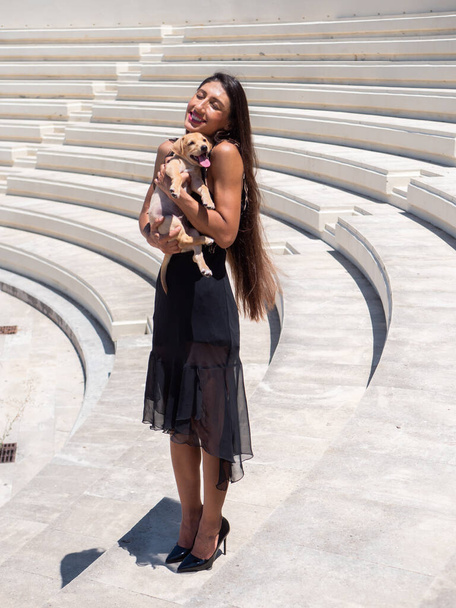 A vertical shot of an attractive female holding a cute dog and posing in an amphitheater - Foto, immagini
