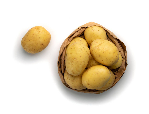 Rauwe hele aardappel stapel geïsoleerd op witte achtergrond bovenaanzicht. Geel gewassen eco bio aardappelen in papieren zak mockup - Foto, afbeelding