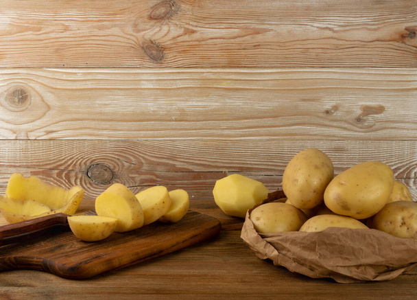 Raw chopped potato mockup with wooden cutting board background. Cut and sliced potatoes on vintage board texture pattern with copy space - Photo, Image