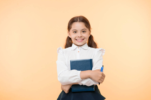 I am ready for school. Child school uniform smart kid done with homework. Girl cute happy face yellow background. Child girl school uniform clothes holds book and pen. Back to school concept - Фото, изображение