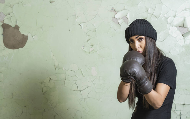 Young girl boxer stands in a protective stance against the background of a green cracked wall - Fotoğraf, Görsel