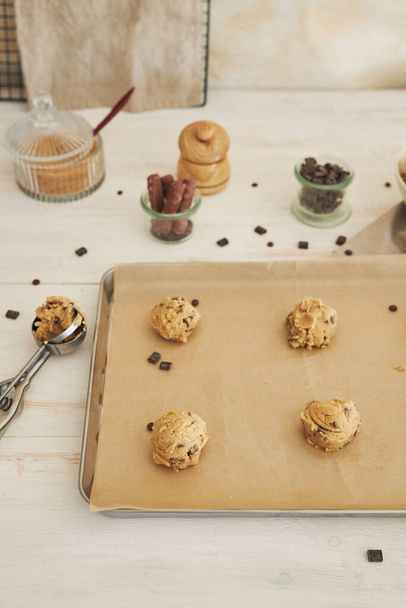 A vertical shot of chocolate chips dough balls on an oven tray - Fotó, kép