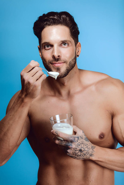 A vertical shot of a topless Caucasian male with an athletic body eating a yogurt - Foto, afbeelding