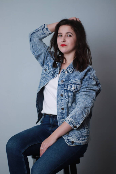attractive brunette in jeans and denim jacket on grey background. studio shoot - Photo, Image