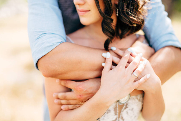 ženich jemně objímá nevěstu zpoza snubního prstenu je na ruce nevěsty - Fotografie, Obrázek