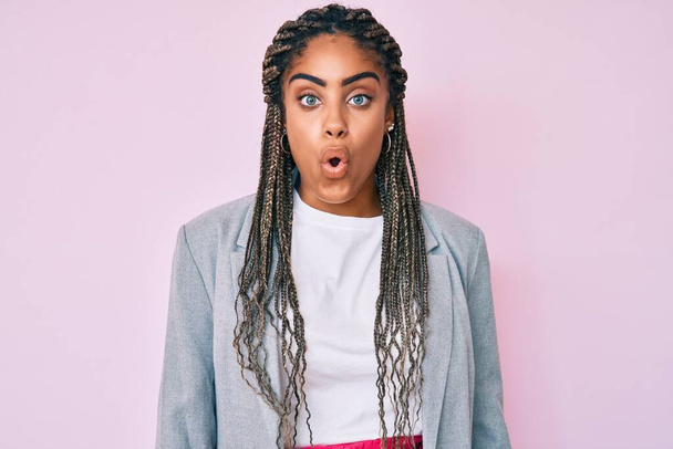 Young african american woman with braids wearing business jacket scared and amazed with open mouth for surprise, disbelief face  - Photo, Image