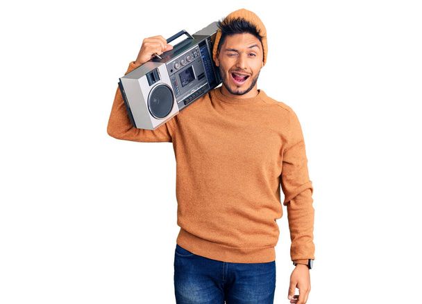Komea latinalaisamerikkalainen nuori mies, joka pitelee boomboxia, kuuntelee musiikin vinkkausta katsomalla kameraan seksikkäällä ilmeellä, iloiset ja onnelliset kasvot..  - Valokuva, kuva