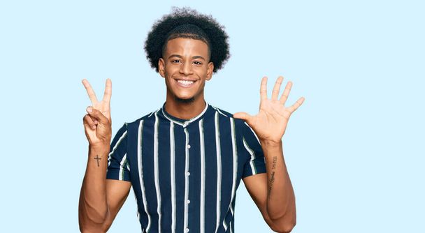 Африканский американец с афроволосами в повседневной одежде показывает и показывает пальцами номер семь, улыбаясь уверенно и счастливо.  - Фото, изображение