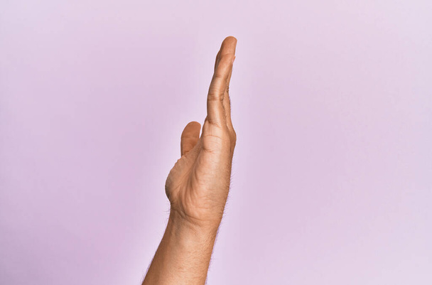 Brazo y mano del joven caucásico sobre fondo rosa aislado mostrando el lado de la mano estirada, empujando y haciendo gesto de parada  - Foto, imagen