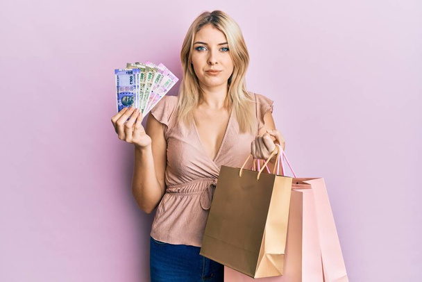 Young caucasian woman holding indian rupee banknotes and shopping bags skeptic and nervous, frowning upset because of problem. negative person.  - Foto, imagen