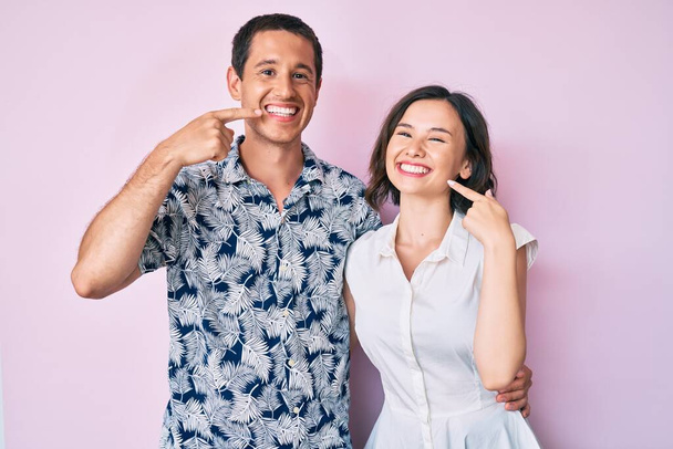 Hermosa pareja vistiendo ropa casual sonriendo alegre mostrando y señalando con los dedos dientes y la boca. concepto de salud dental.  - Foto, imagen