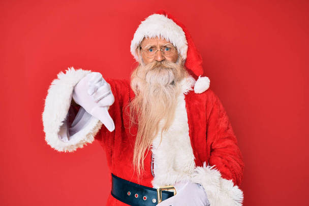 Old senior man with grey hair and long beard wearing traditional santa claus costume looking unhappy and angry showing rejection and negative with thumbs down gesture. bad expression.  - Fotoğraf, Görsel