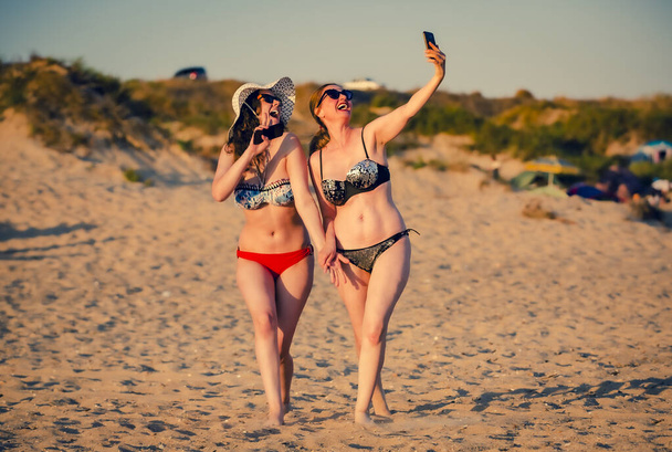 Mother and daughter make selfie on beach smiling and making funny faces. Mother and daugher teen brunettes are taking pictures with mobile phones on the beach. - Φωτογραφία, εικόνα