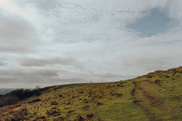 緑の道は、晴れた秋の日にイギリスのサマセット州メンディップヒルズの丘を登っています。人の距離で水平線の上を歩くシルエット。スペースのコピー. - 写真・画像