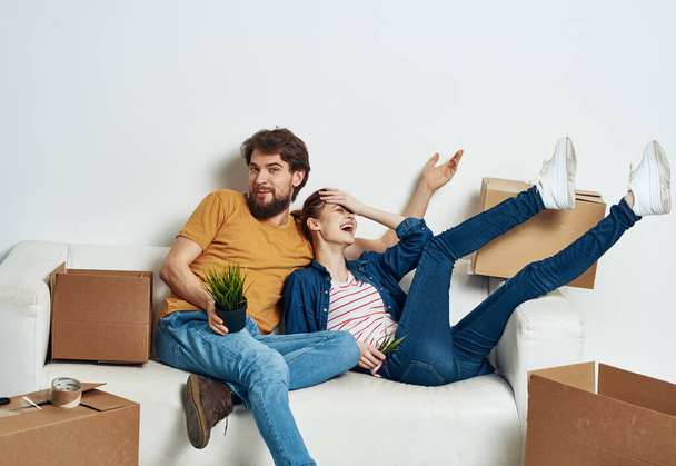 Мужчина и женщина сидят на диване рядом с коробками с вещами, перемещающими интерьер комнаты - Фото, изображение