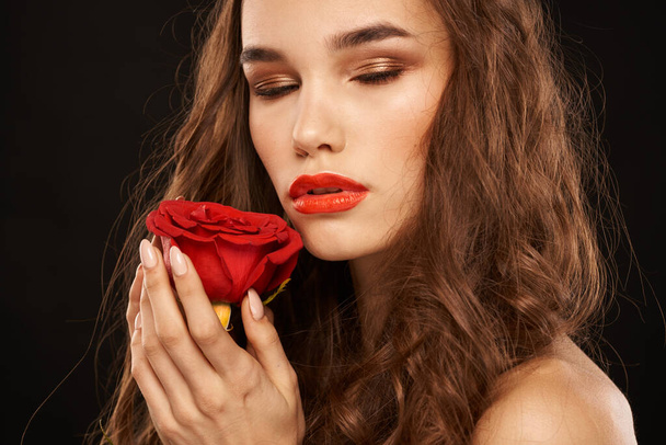 femme avec une rose rouge sur un fond sombre cheveux longs maquillage lèvres rouges - Photo, image