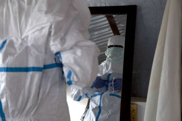 Lunsar, Sierra Leona - 29 de abril de 2015: Trabajador de la salud africano se prepara y se pone ropa protectora del EPP durante el brote de ébola. Contexto epidémico y covid - Foto, imagen