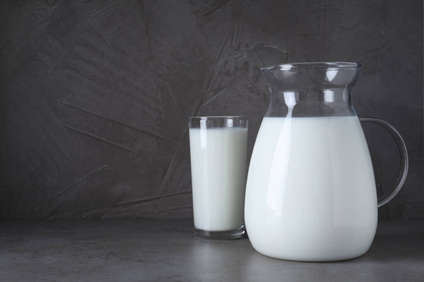Caraffa e bicchiere con latte fresco sul tavolo grigio. Spazio per testo - Foto, immagini