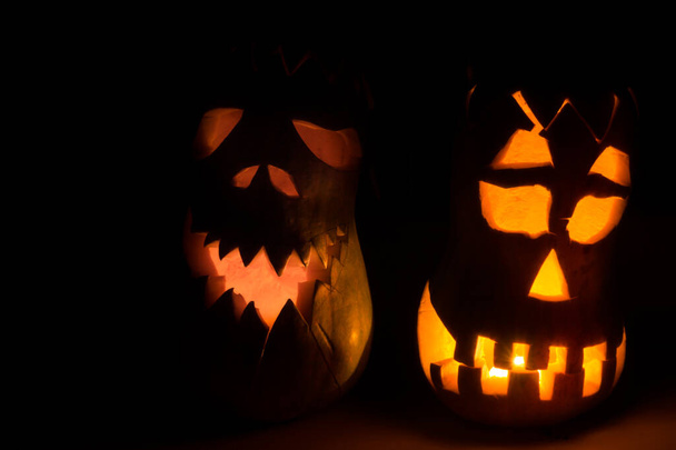 Two evil pumpkins for Halloween. An evil face is carved on the pumpkin, a candle is burning inside, in a dark room. - Photo, Image