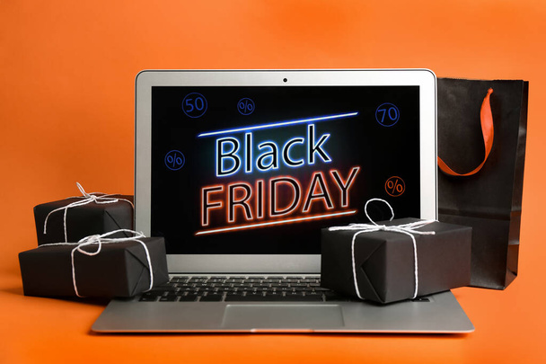 Laptop with Black Friday announcement, shopping bag and gifts on orange background - Foto, Imagem