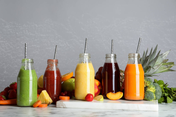 Bottles of delicious juices and fresh fruits on white marble table - Valokuva, kuva