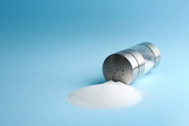 Scattered salt and shaker on light blue background, closeup. Space for text - Foto, imagen