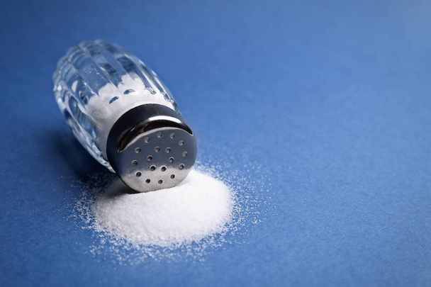 Scattered salt and shaker on blue background, closeup. Space for text - Φωτογραφία, εικόνα