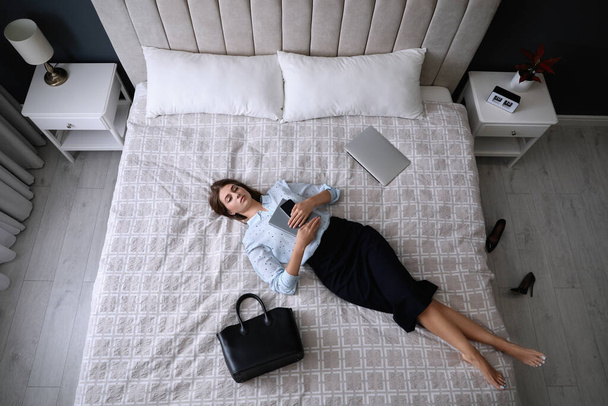 Exhausted businesswoman in office wear sleeping on bed at home after work, above view - 写真・画像