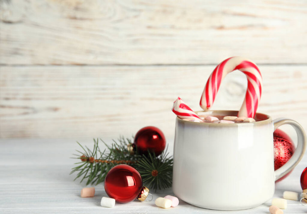 Cup of tasty cocoa with marshmallows, candy cane and Christmas decor on white wooden table. Space for text - Foto, Bild