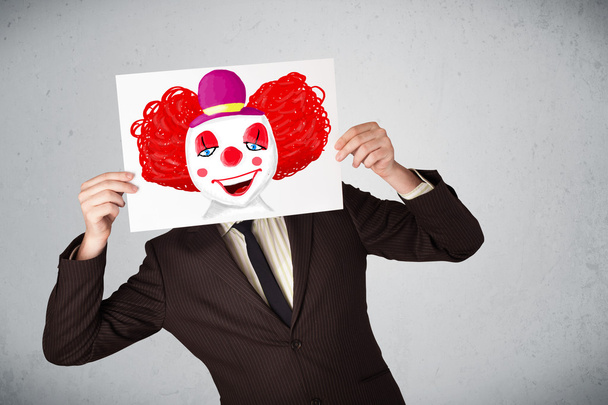 Businessman holding a cardboard with a clown on it in front of h - Foto, Imagen