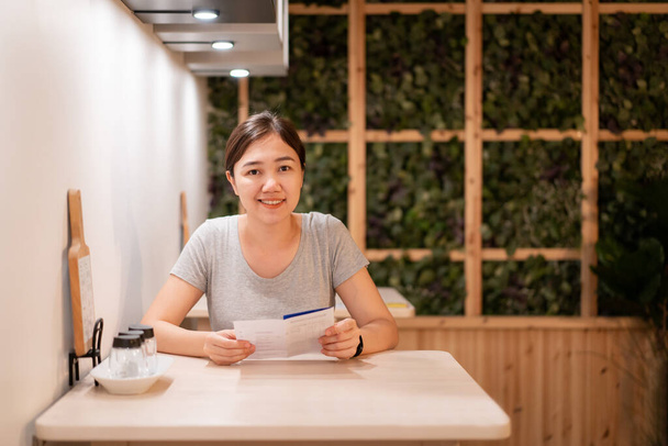 Beautiful Asian woman looking the menu in the small restaurant with copyspace. Cheerful Asian woman waiting for a food in the restaurant. - Fotoğraf, Görsel