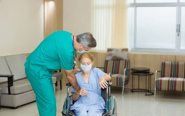 Медбрат толкает инвалидное кресло пожилой женщины в больничном коридоре, чтобы расслабиться, выздоравливая после болезни.. - Фото, изображение