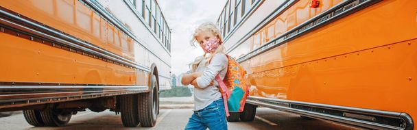 Кавказька дівчинка-підліток в масці стоїть біля жовтого шкільного автобуса. Система освіти і повернення до школи у вересні. Нова нормальна під час коронавірусу covid-19. Веб-банер. - Фото, зображення