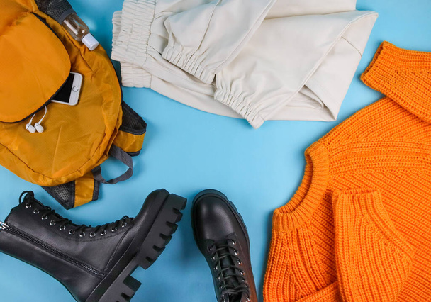 Sweater, backpack, pants and boots lie in a circle on a blue background with space for text in the middle, top view close-up. - Photo, Image