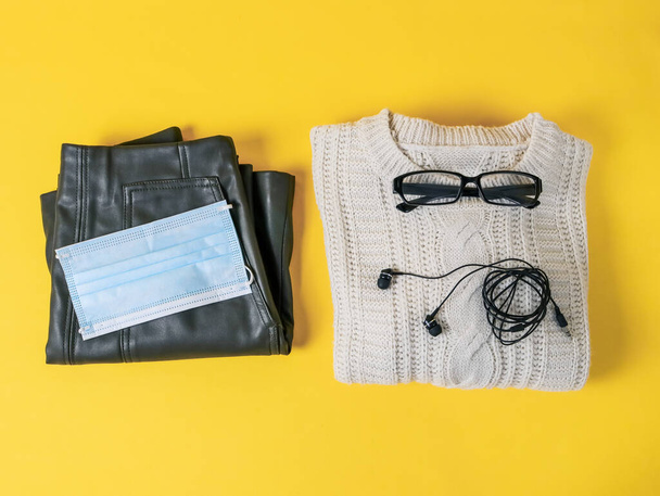 Skirt, sweater, glasses, headphones and a medical mask on a yellow background, close-up top view. - Valokuva, kuva